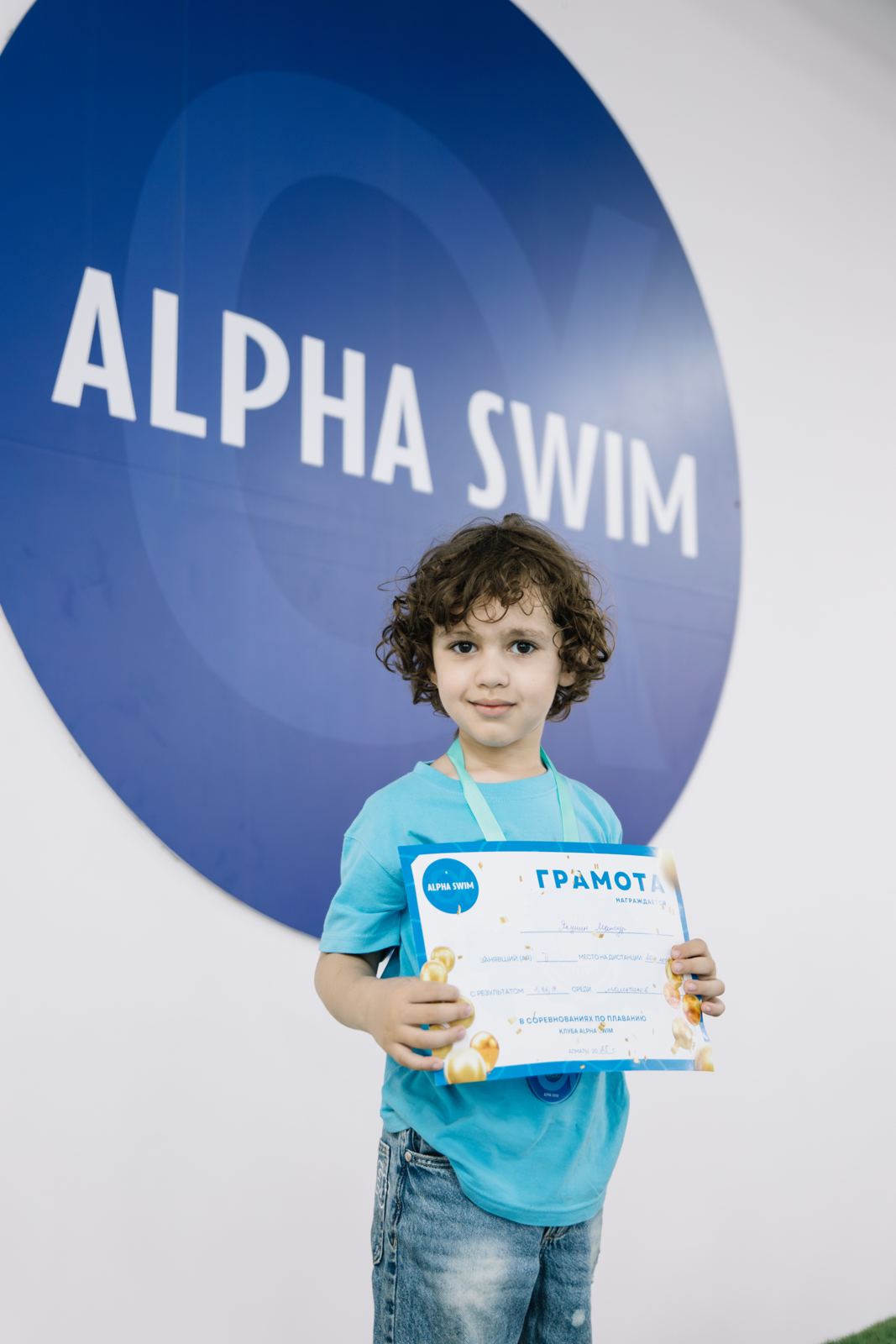 Мальчик с грамотой у логотипа Alpha Swim